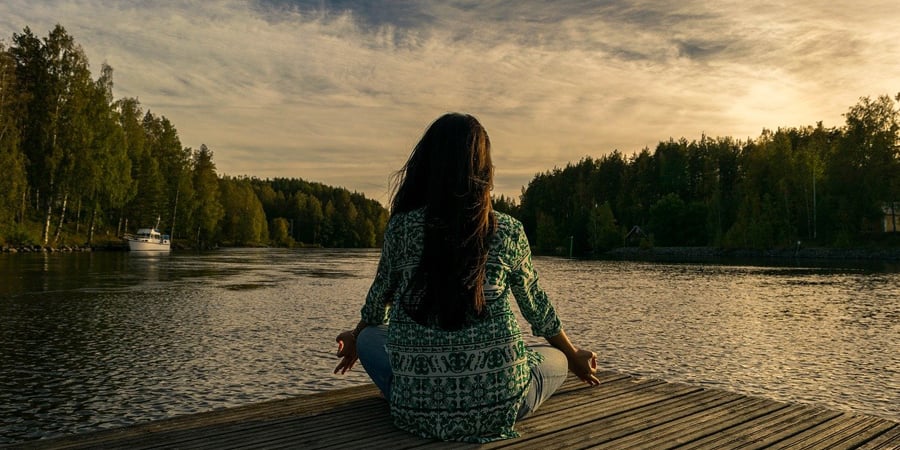 woman meditating on dock of lake