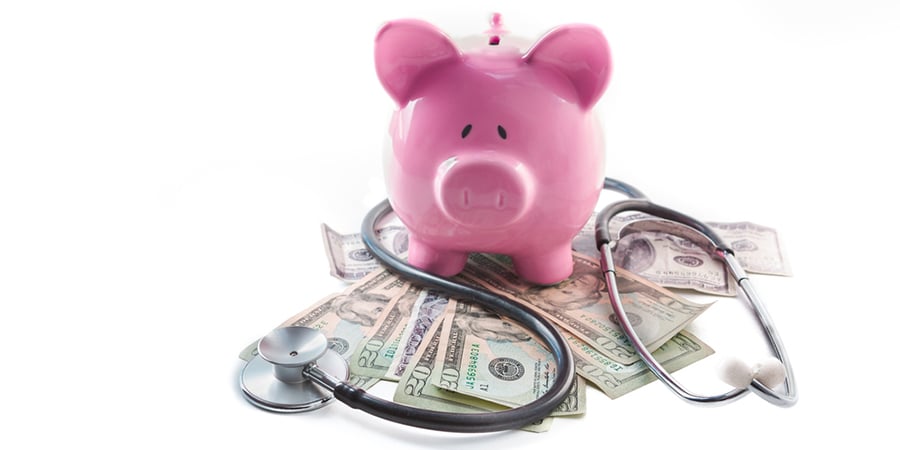Piggy bank and stethoscope resting on pile of dollars on white background